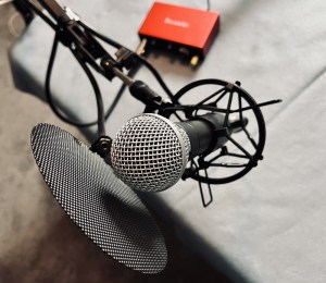 A dynamic microphone with a pop filter attached to an arm and connected to a red pre-amp.