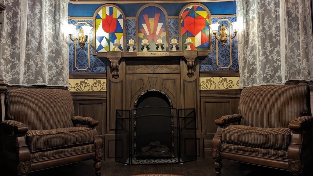 An ornate, old living room with stained glass windows over a wooden fireplace.