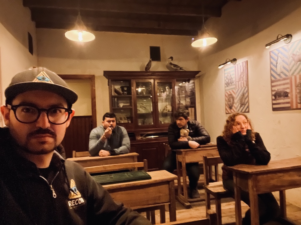 A selfie with 4 players seated at wooden school desks. In the background is a breakfront.