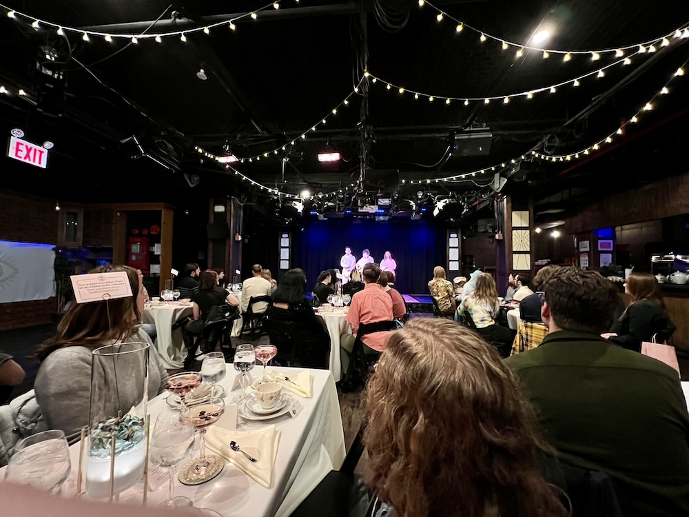Wide shot of the audience of Order of the Golden Scribe watching the cast on stage.