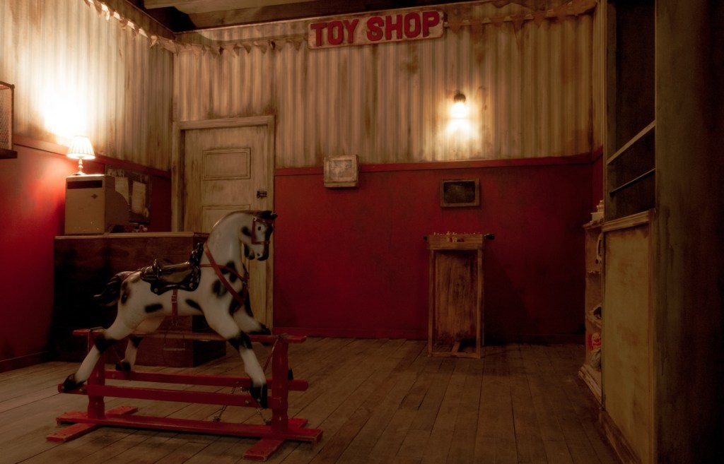 An old, rundown toy shop with an assortment of old toys. A rocking horse sits in the middle of the store.