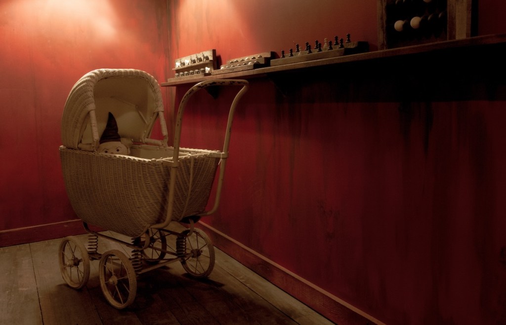 A toy baby carriage with a doll in it beside a shelf with some games.