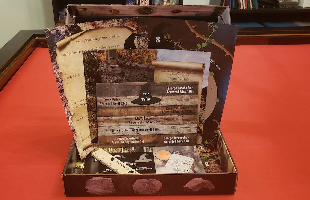 Escape The Crate game box open with the Witch Trials components inside.