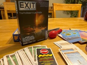 A game box sits on a table, in front of it are game cards and paper game components.