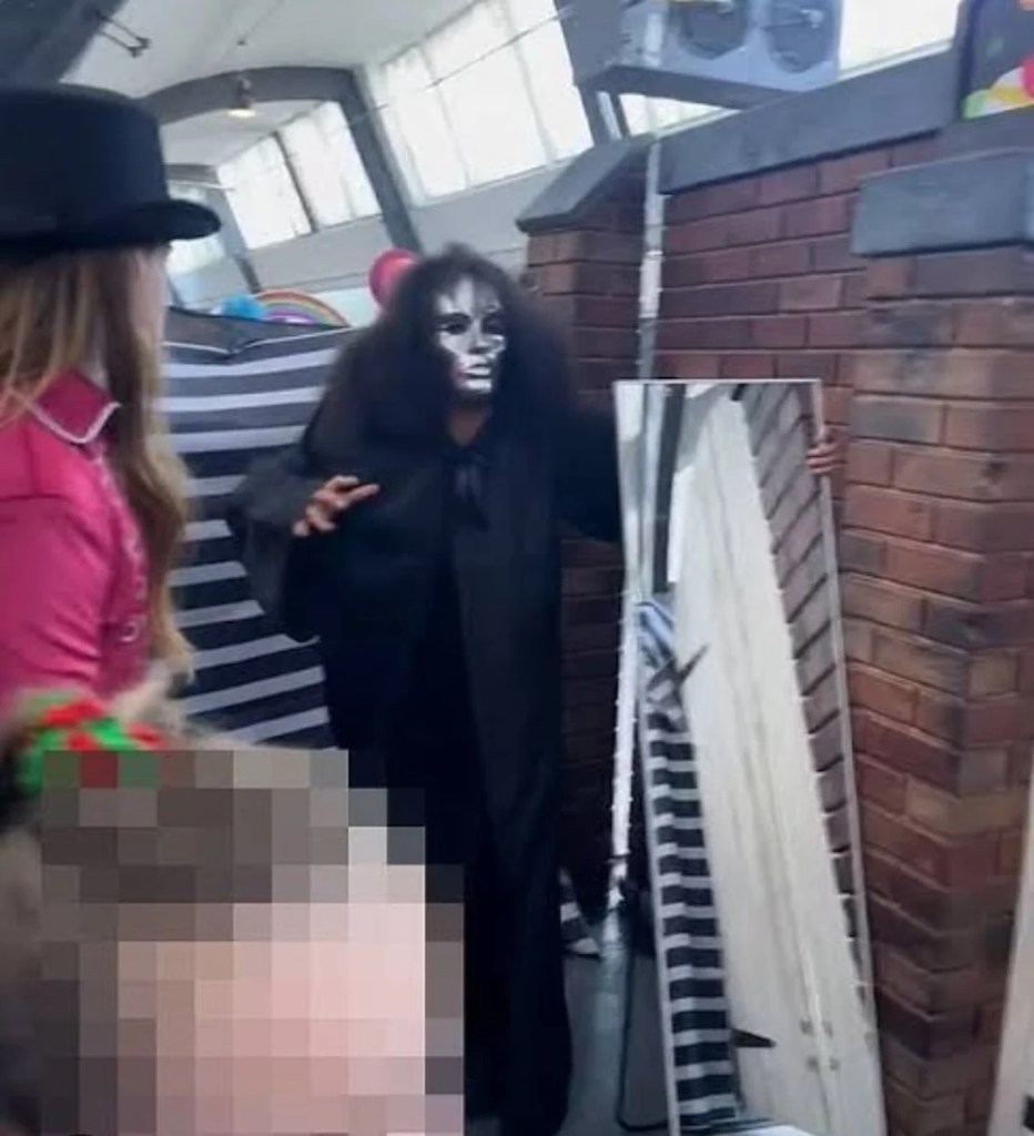 A scary, silver-masked character cloaked in black approaching a parent and their child.