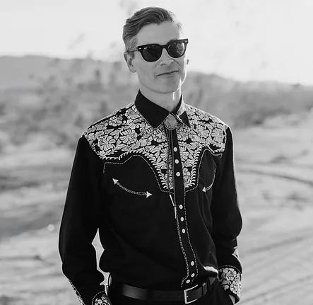 black and white image of man in cowboy shirt and sunglasses standing in the desert