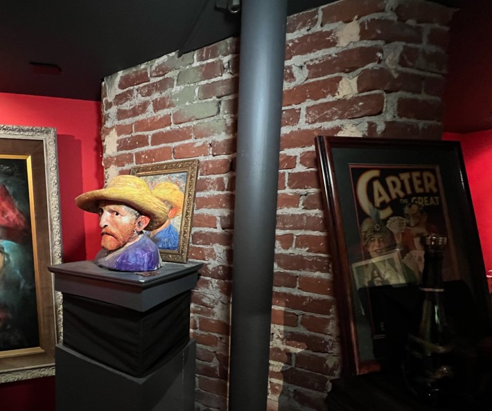 sculpture of van gogh head against a brick wall, there is a framed poster leaning on wall also