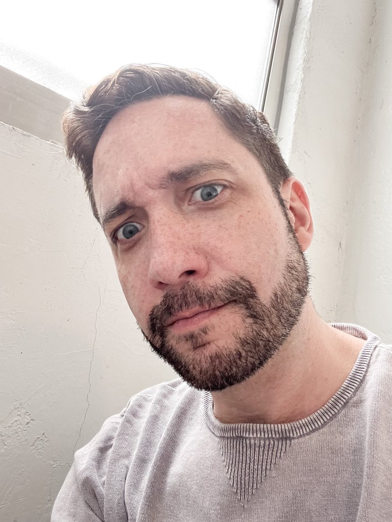 close up of a man with brown hair and blue eyes and a short beard staring down at the camera intently
