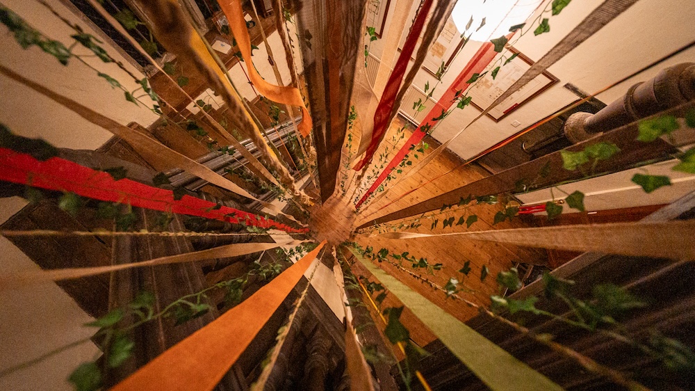 View down a stairwell, through drapped ribbon and vine.
