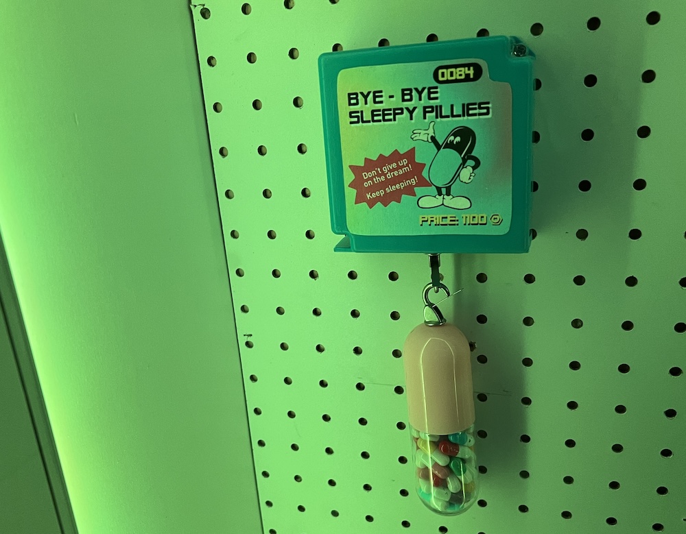 Closeup of an item for sale, "Bye-Bye Sleepy Pillies" An anthropomorphized pill says, "Don't give up on the dream! Keep Sleeping!"