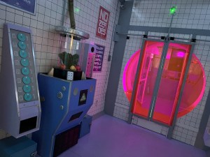 Wide view of 2084 with an assortment of strange devices and a large pink doorway.