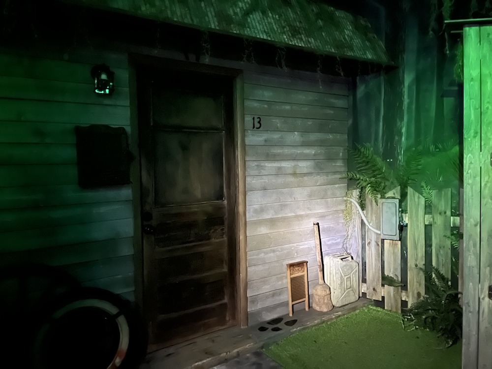 Exterior of an old, rundown cabin, bathed in green light.
