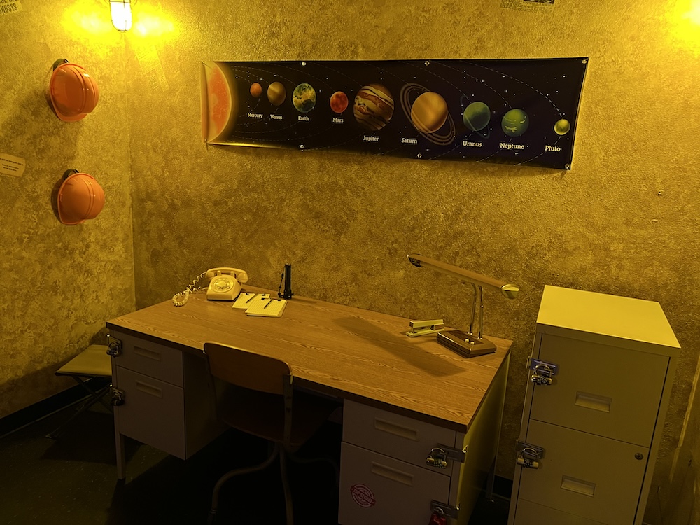 A desk with many padlocks on it, below a depiction of the Earth's Solar System.