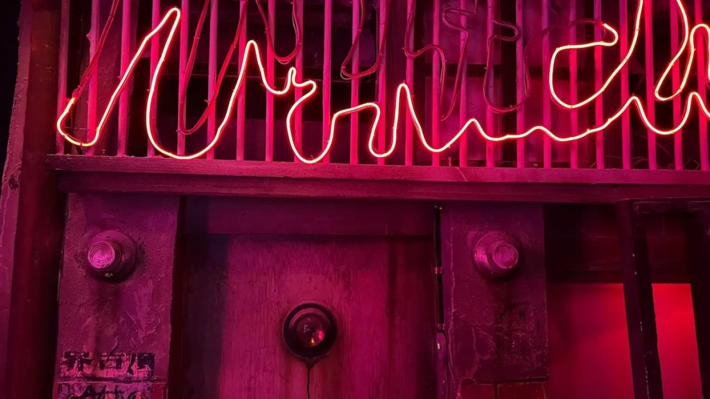 A locked storefront in a cyberpunk world with pink LED signage that is partially dead.