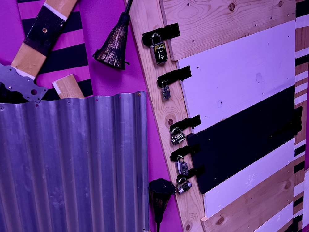 A door locked with 5 different padlocks. The door and surrounding area are decorated with an assortment of wood and metal scraps.