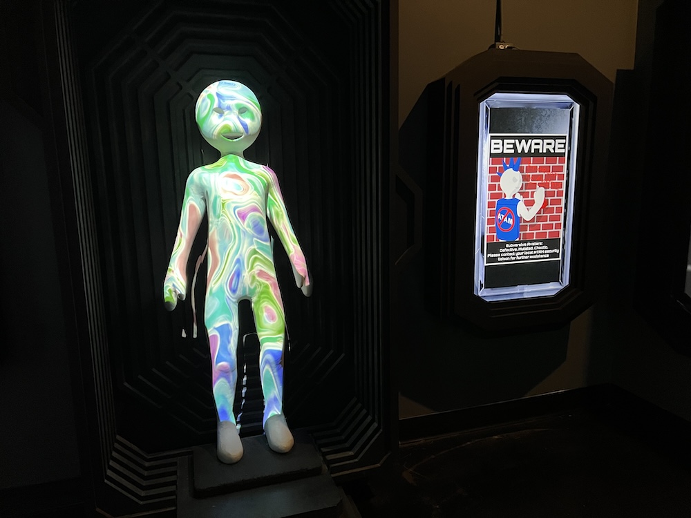 A projection mapped alien beside a Beware sign.