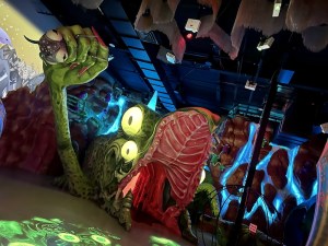 A massive green monster with long, painted nails, holding a small monster, with an open mouth that you can walk into.