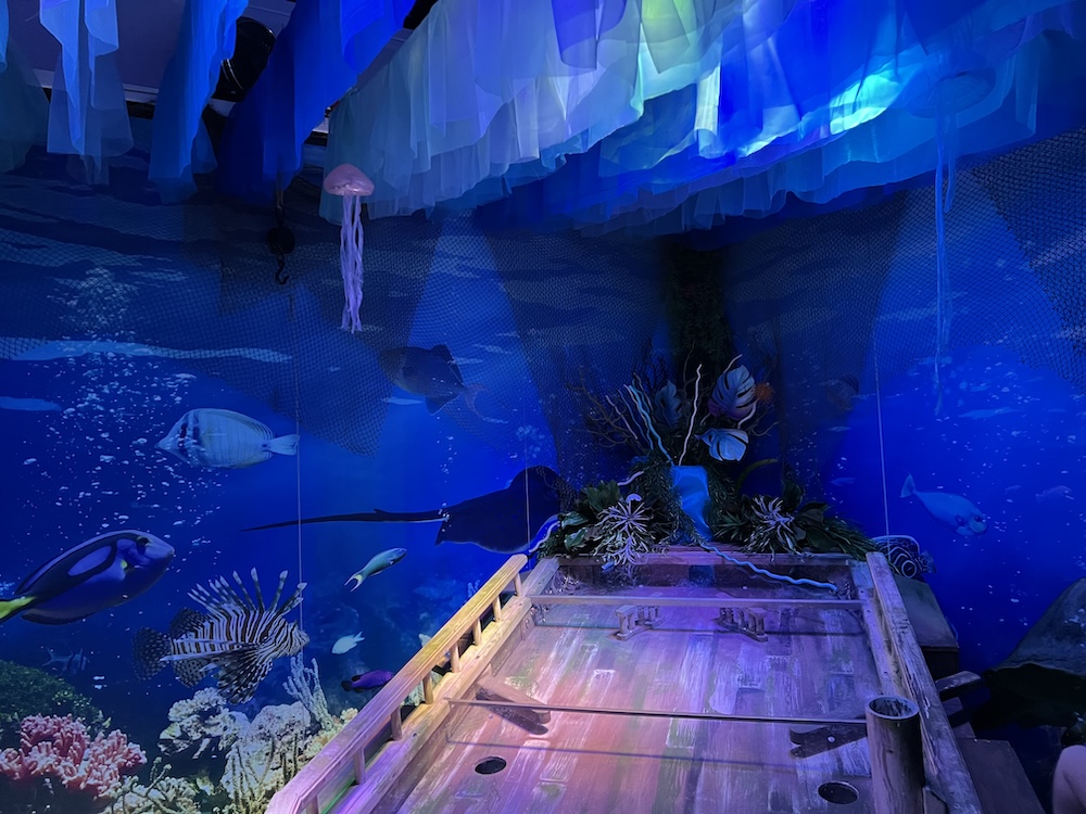 A large wooden, hand-powered pinball machine that looks like a shipwreck in the middle of an ocean scene.