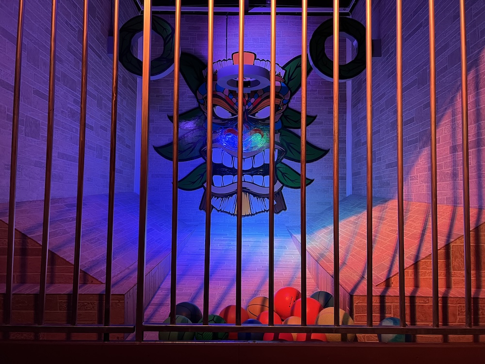 A Mayan themed ball toss game viewed through a cage door.