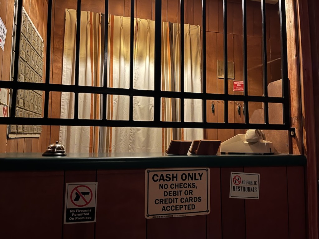 A motel front desk with a gate. A sign reads, "Cash Only."