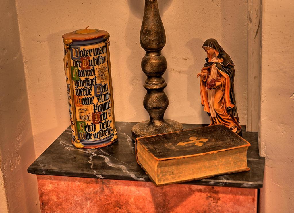 A bible, statue of the Virgin Mary, a light, and a candle on a small table.