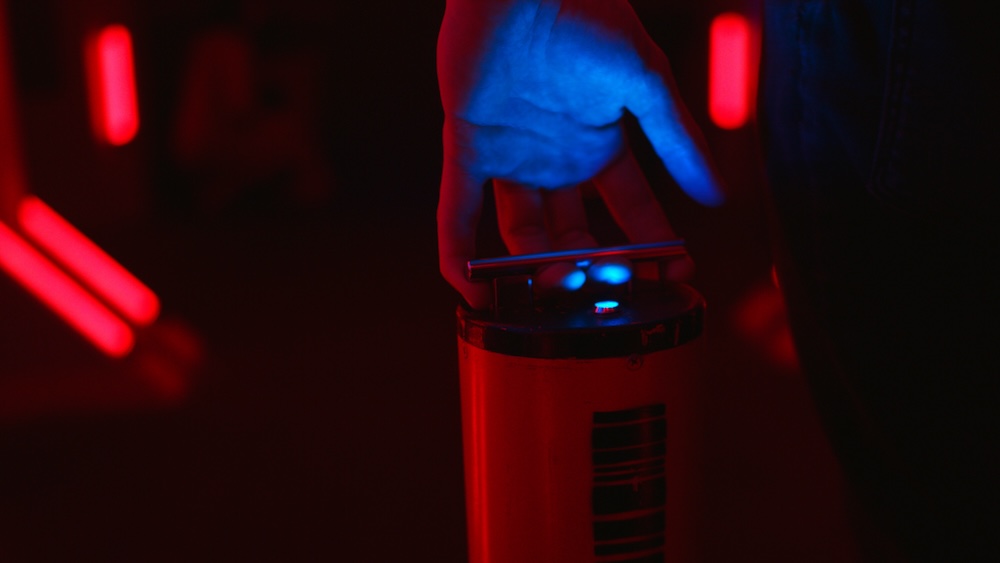 A hand holding a futuristic battery in a dramatically lit, sci-fi environment.