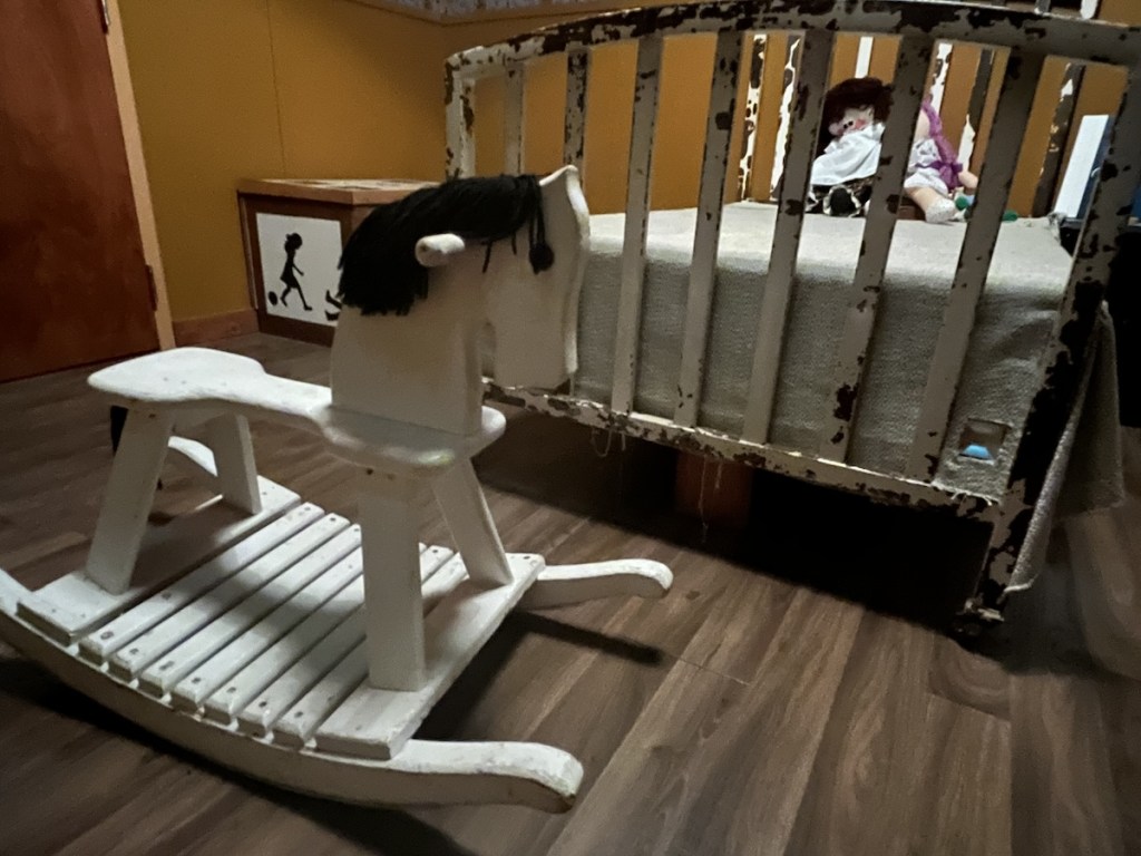 A rocking horse at the foot of a beat up, old, children's bed.