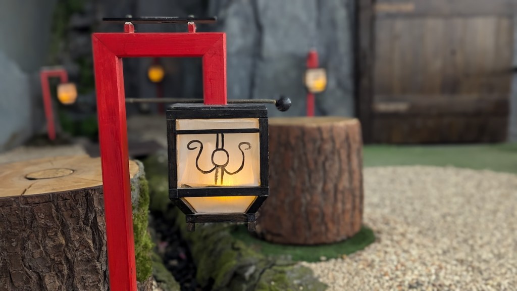 A small lantern on a red mount beside a few tree stump seats.