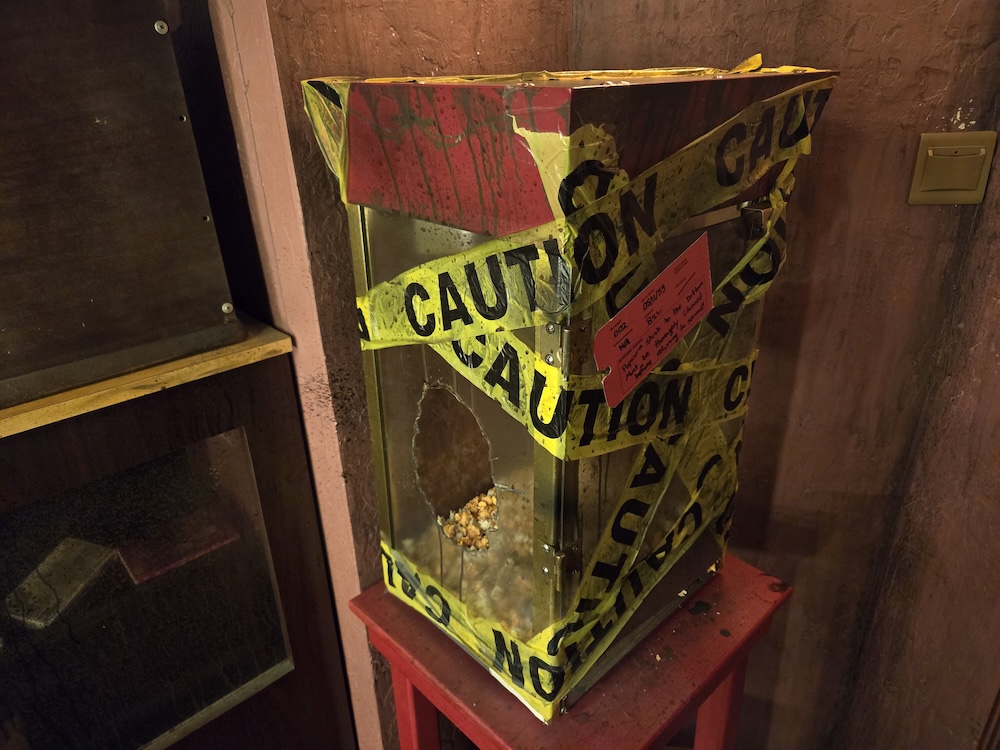An old, gross movie popcorn machine with broken glass, wrapped in caution tape.