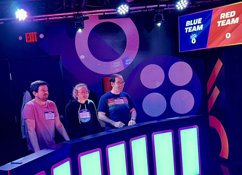 Jorge, Lisa, and Evan behind the blue podium at the start of Great Big Game Show.