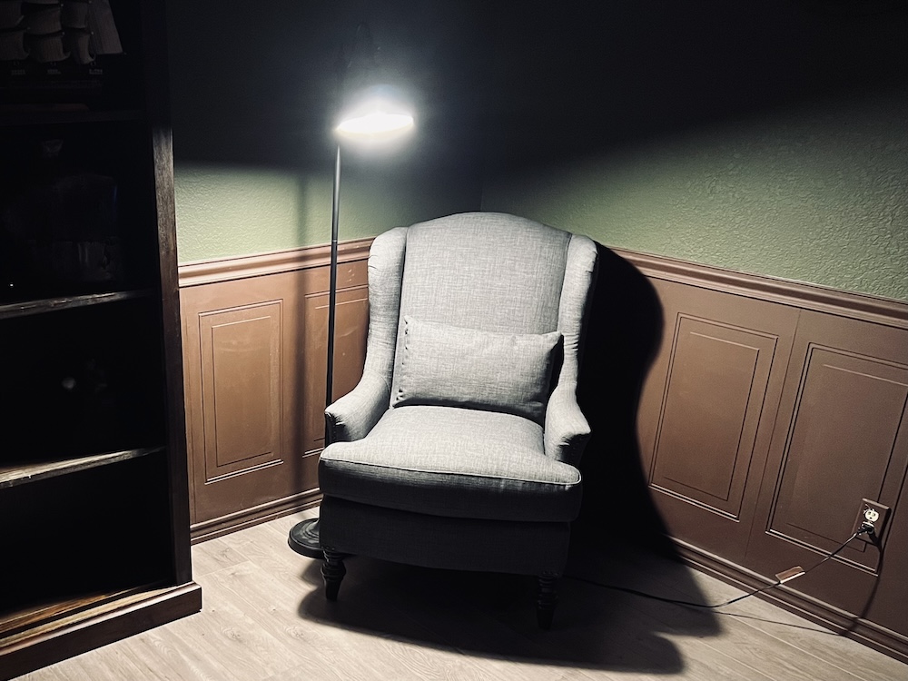 A large, soft chair in the corner of a bare apartment. A floor lamp illuminates it.