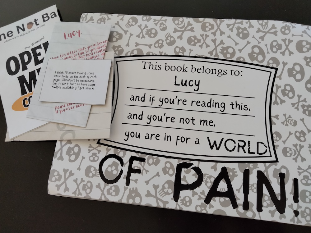 Some papers next to the inside cover of a scrapbook, which reads "This book belongs to Lucy and if you're reading this, and you're not me, you are in for a WORLD OF PAIN!"