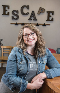 Woman smiling, long curled blond hair, wearing glasses and a denim jacket.