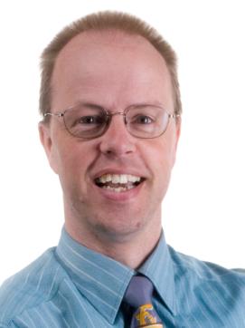 man with short blond hair, wearing glasses, in a striped blue shirt and tie.