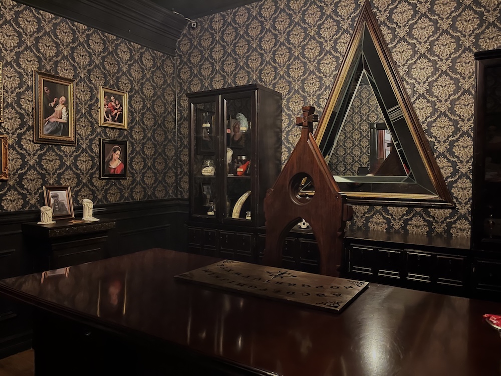 A study for some kind of christian cleric. A spirit board, melted candles, a large chair with a cross, a case with religious relics, and old paintings.