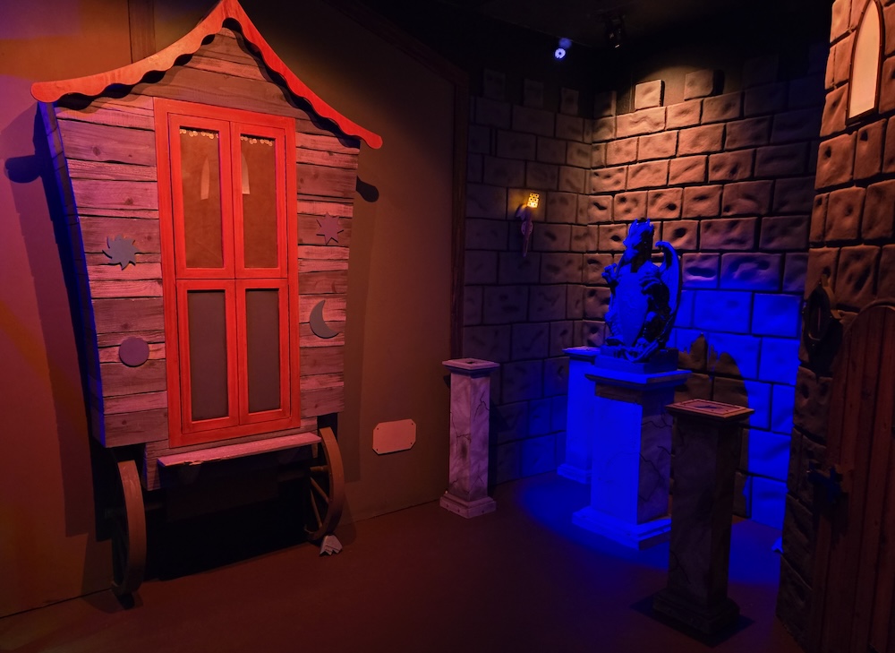 The rear of a wagon beside a castle wall with a dragon statue.