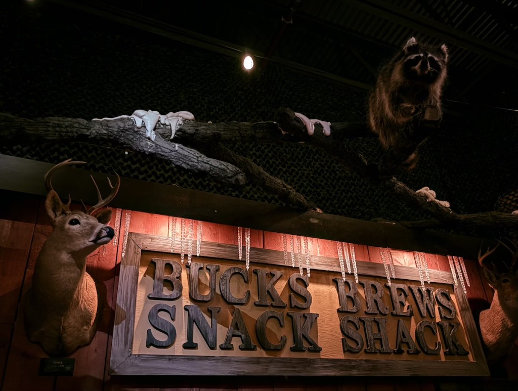 "Bucks Brews Snack Shack" with taxidermy bucks hung beside the sign. A racoon hangs from the roof.