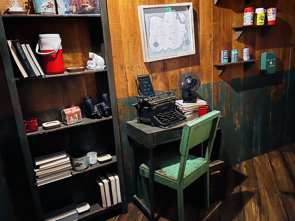 A small office with an old typewriter, and assorted books, beverages, and equipment fot surviving the arctic.