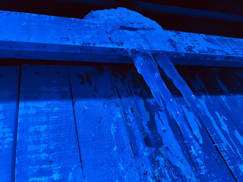 Stalactites of ice hanging from the side of a wood building.