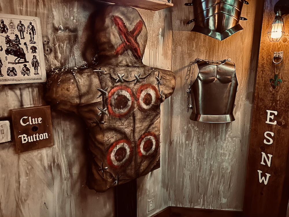 A burlap combat practice dummy shaped like a person with targets on its body, beside armor plates.