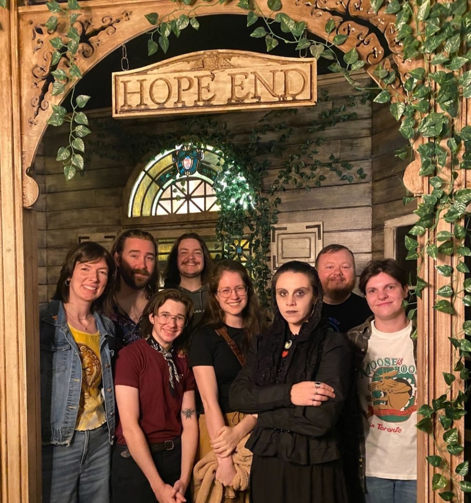 The first Play More Games cohort o the front porch of Hope End, a ghostly character standing with them.