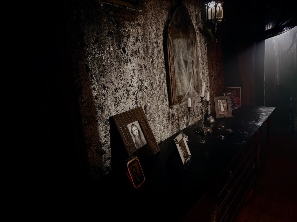 A small table with an assortment of photos and a candelabra. Behind it is a cob-webbed mirror.