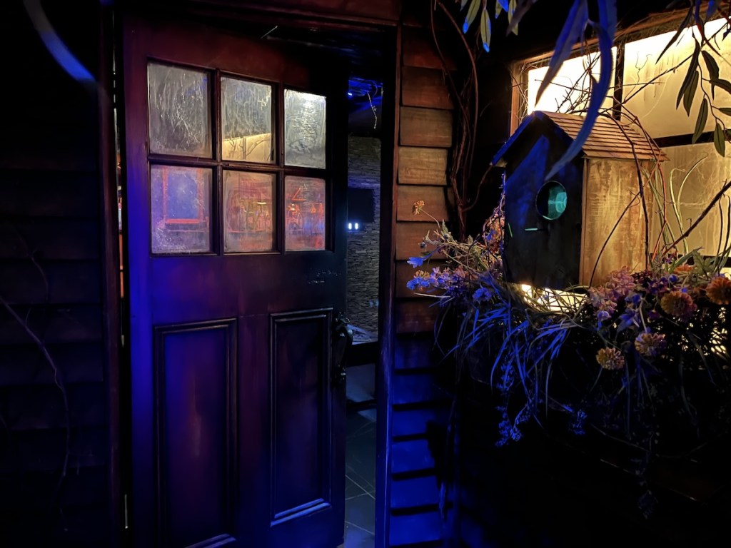 A dimly lit entrance to a house. Beside the door is a planter with a large birdhouse on it.