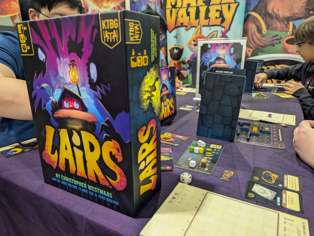 A close up image of the box for the board game Lairs, and one player's board setup of the same game.