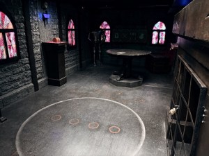The interior of a castle, with stained glass windows on all sides and a large white circle, with 4 small orange circles on the floor.