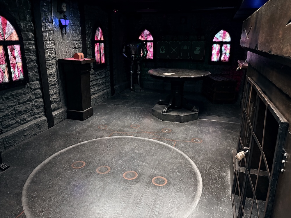 The interior of a castle, with stained glass windows on all sides and a large white circle, with 4 small orange circles on the floor.