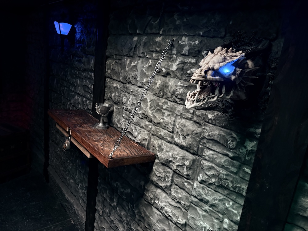 Stone castle walls with a dragon grotesque with glowing blue eyes hanging from the wall.