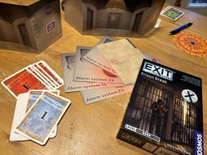 Exit The Game Prison Break box depicting a prison cell beside an assortment of game components including cards, and alarm system files.