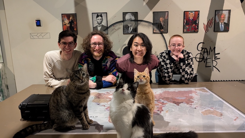 Team photo in a room with a map of the world on a table, many cats sit atop it. In the background are portraits of US Presidents with cat ears.