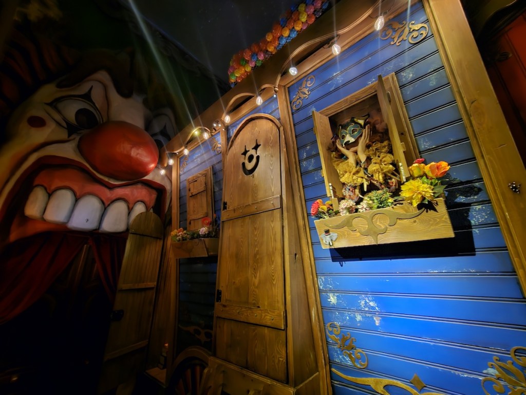 A clown in a wolf costume looking out of the window of a circus caravan.